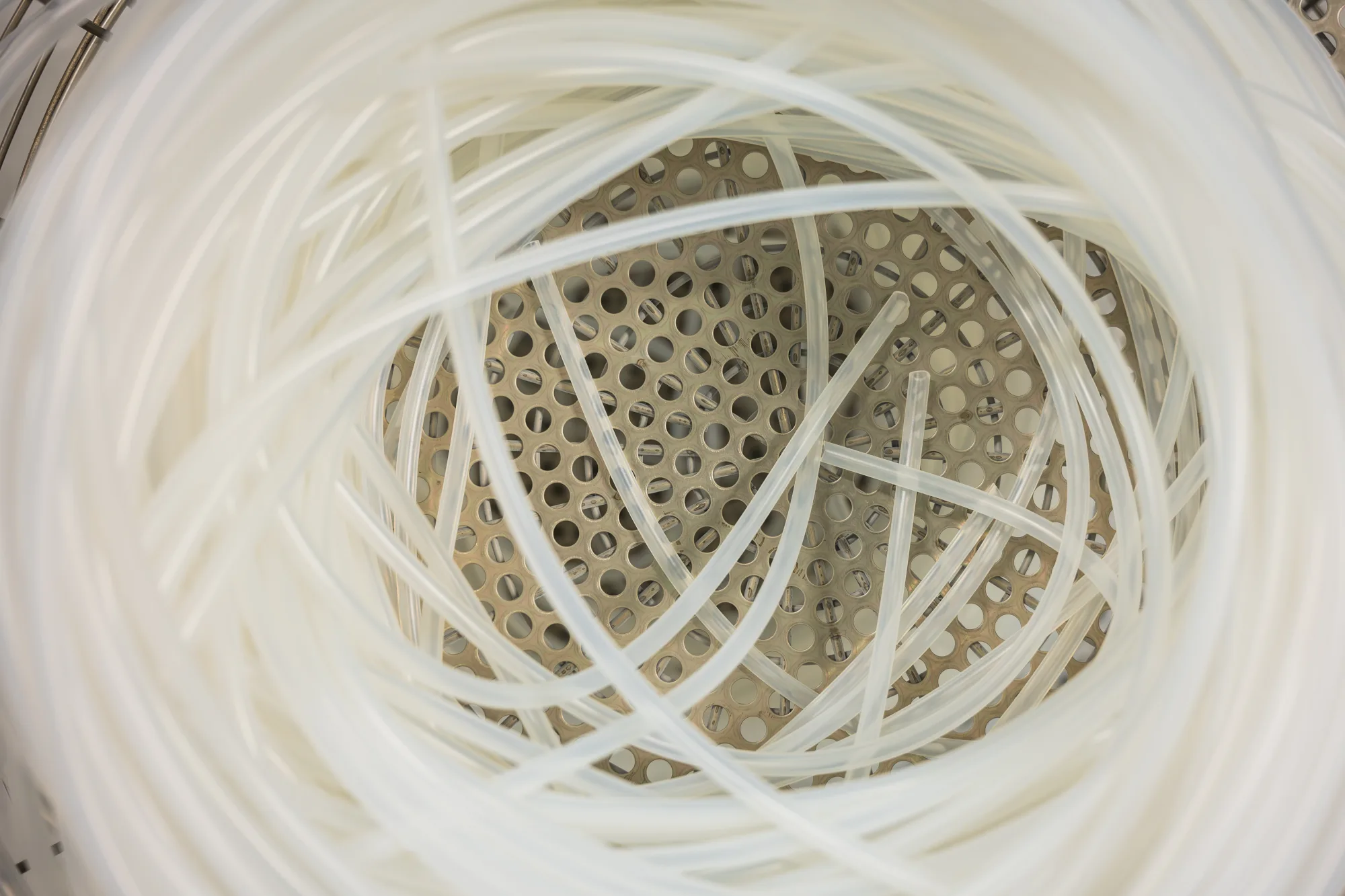 Coil of fine medical tubes stored in a perforated steel basket · top view.