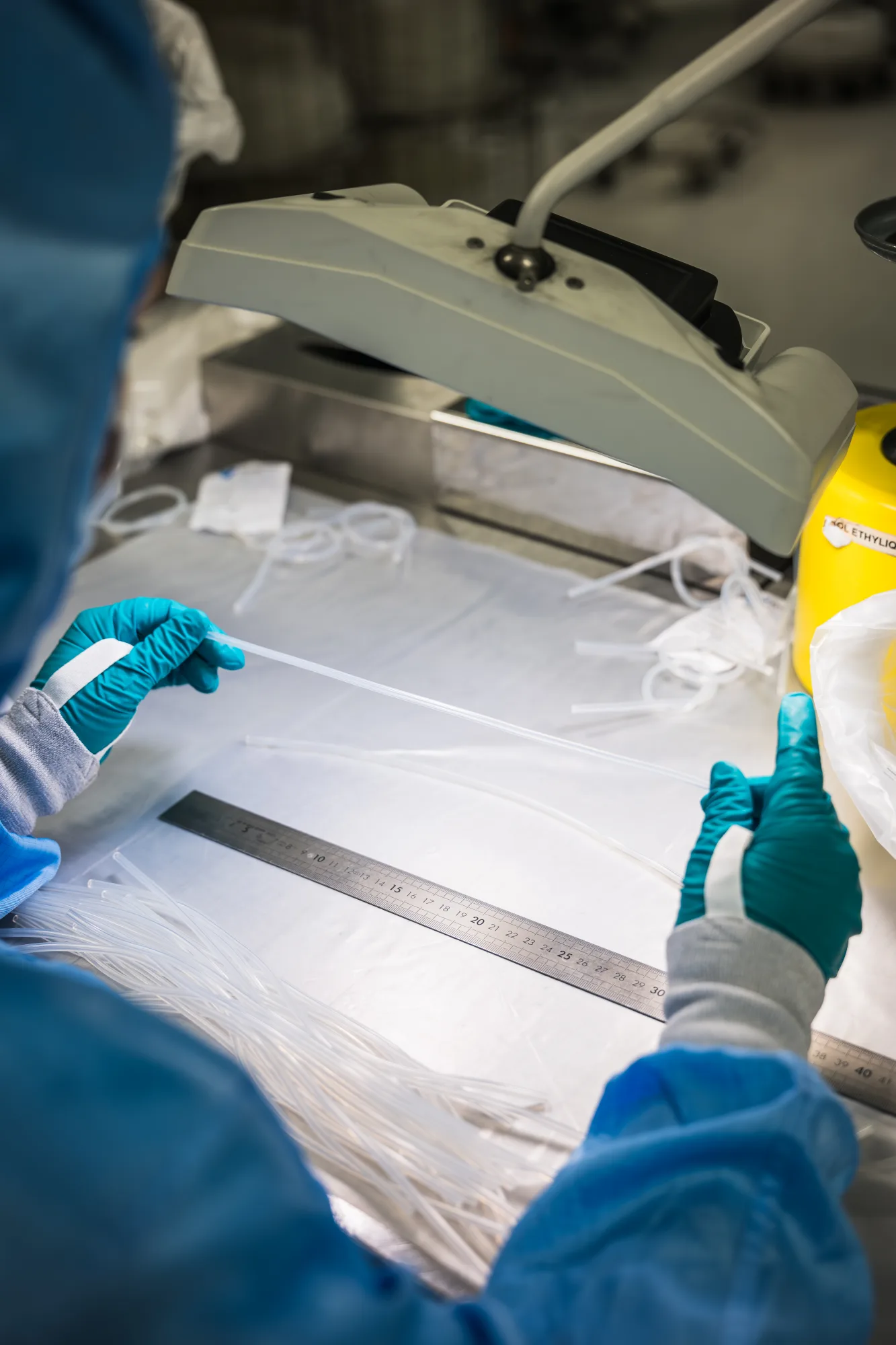 Visual inspection of fine medical tubes on a control bench with a metal ruler.